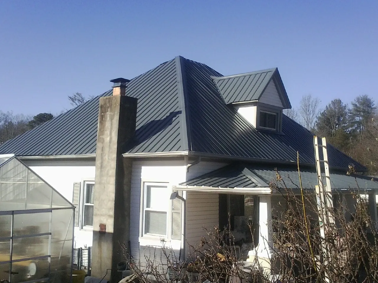 Dark blue standing seam metal roof on a white farmhouse with dormer — Slate & Tile Roof Repair by Roofing Brothers in Creola