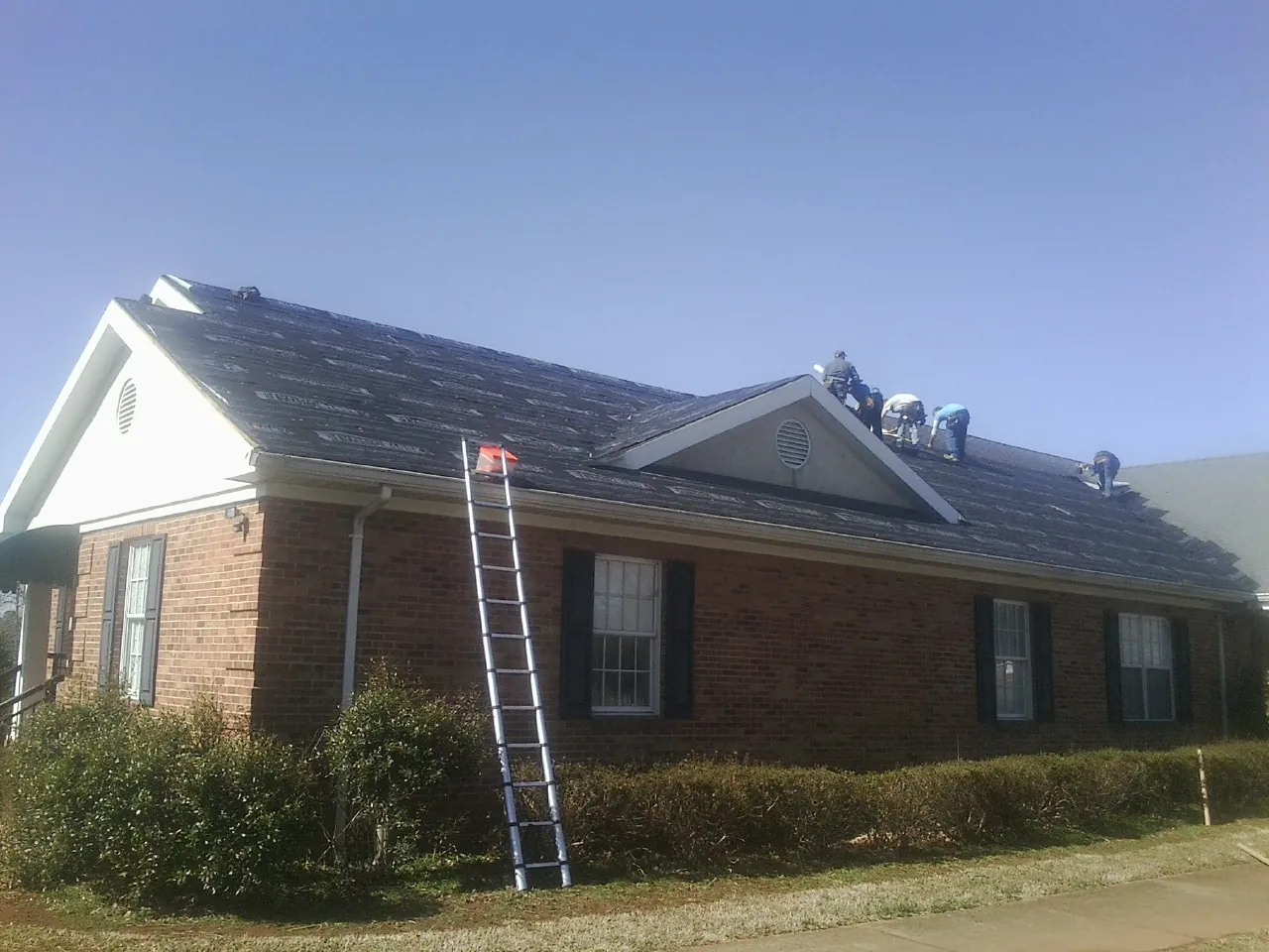 Crew tearing shingles off a brick ranch roof with a ladder set — Metal Roof Repair work by our crew in Creola