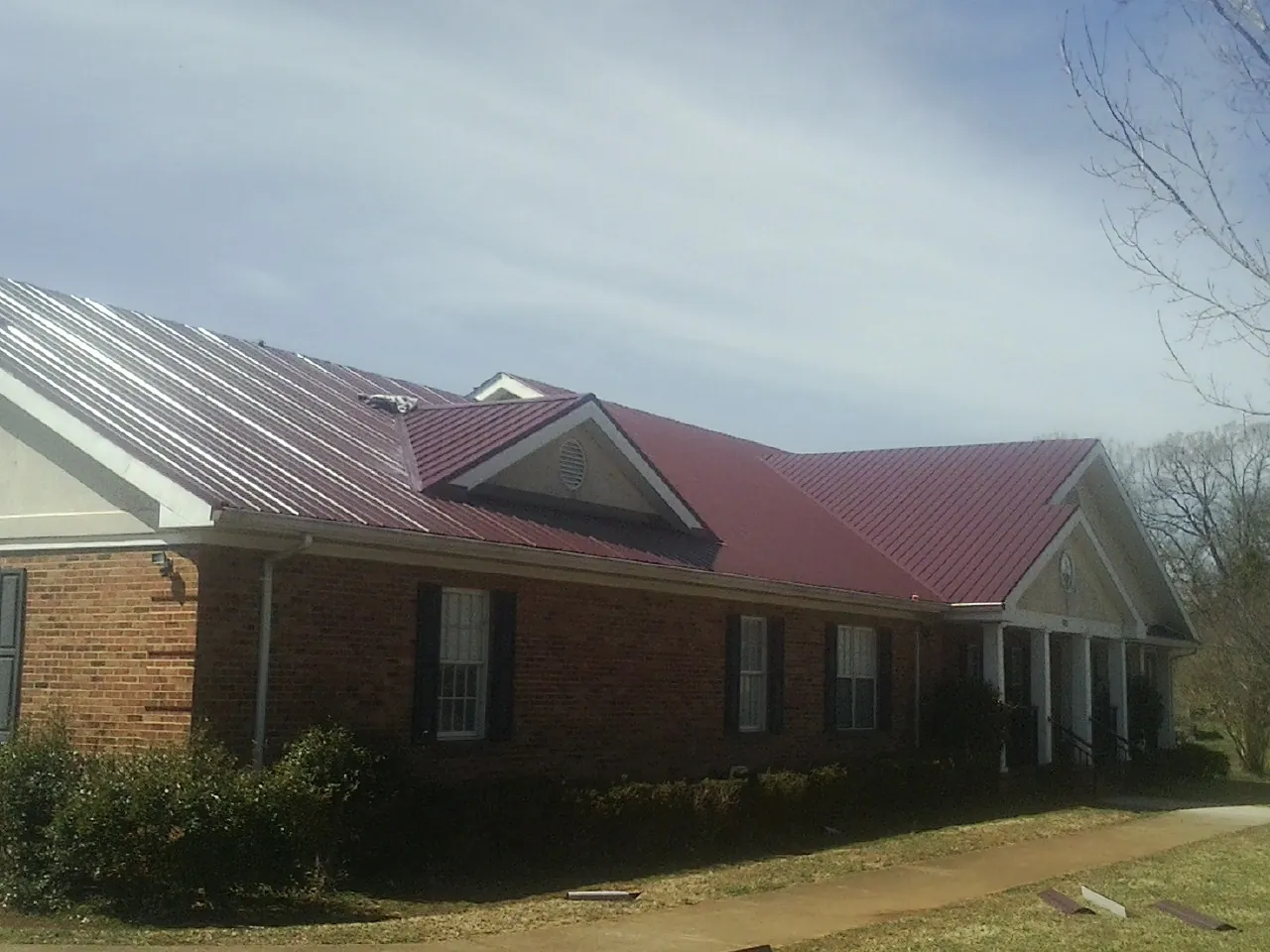 Red metal roof with gabled entries on a long brick building, from a Hail Damage Roof Repair job in Creola
