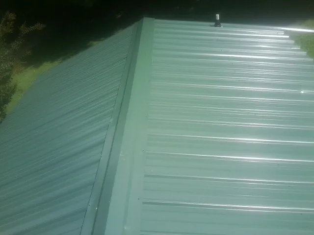 New green metal panels meeting at the ridge of a roof — Flat Roof Repair work by our crew in Creola