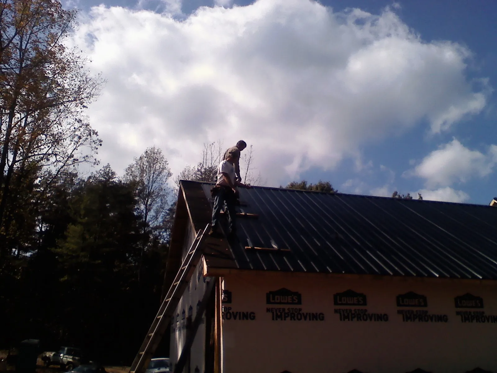 Roofer fastening dark metal panels high against a cloudy sky, from a Roof Inspection job in Creola