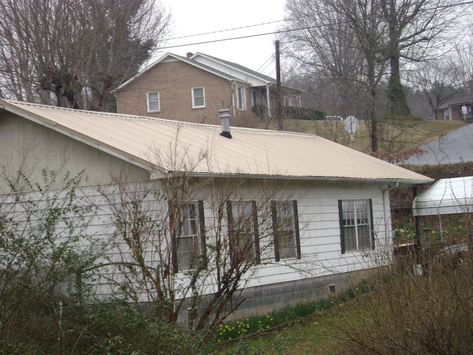 Tan metal roof on a white sided house set into a hillside — Commercial Roofing by Roofing Brothers in Creola